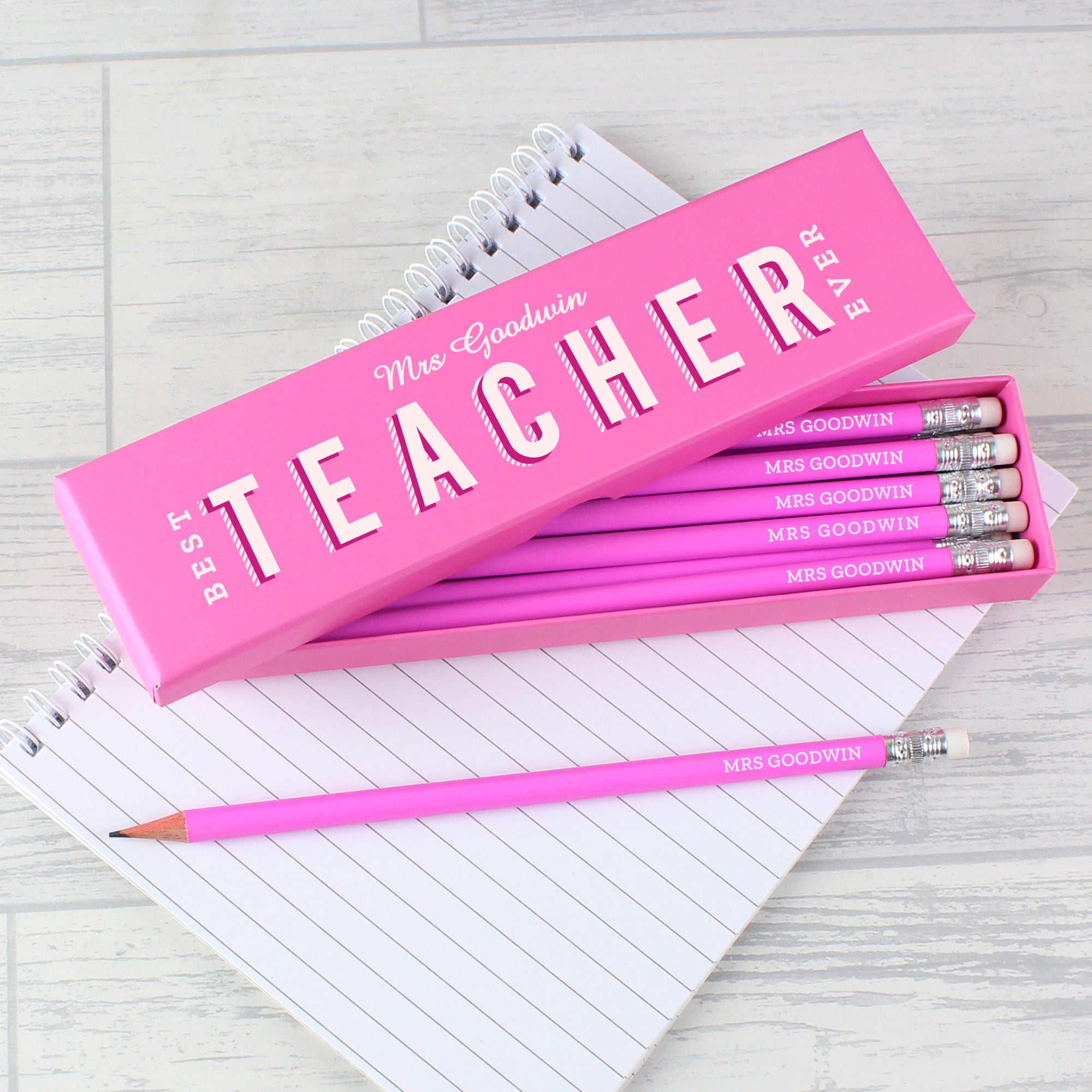 Image of a personalised box containing 12 personalised pencils. The box is pink and can be personalised with a teacher’s name which will be followed by the fixed text of Best Teacher Ever which is printed in white modern uppercase letters. Inside the box has 12 HB pencils with a pink outer and a small eraser at the end. Each pencil will also be personalised with the teacher’s name in white uppercase letters.