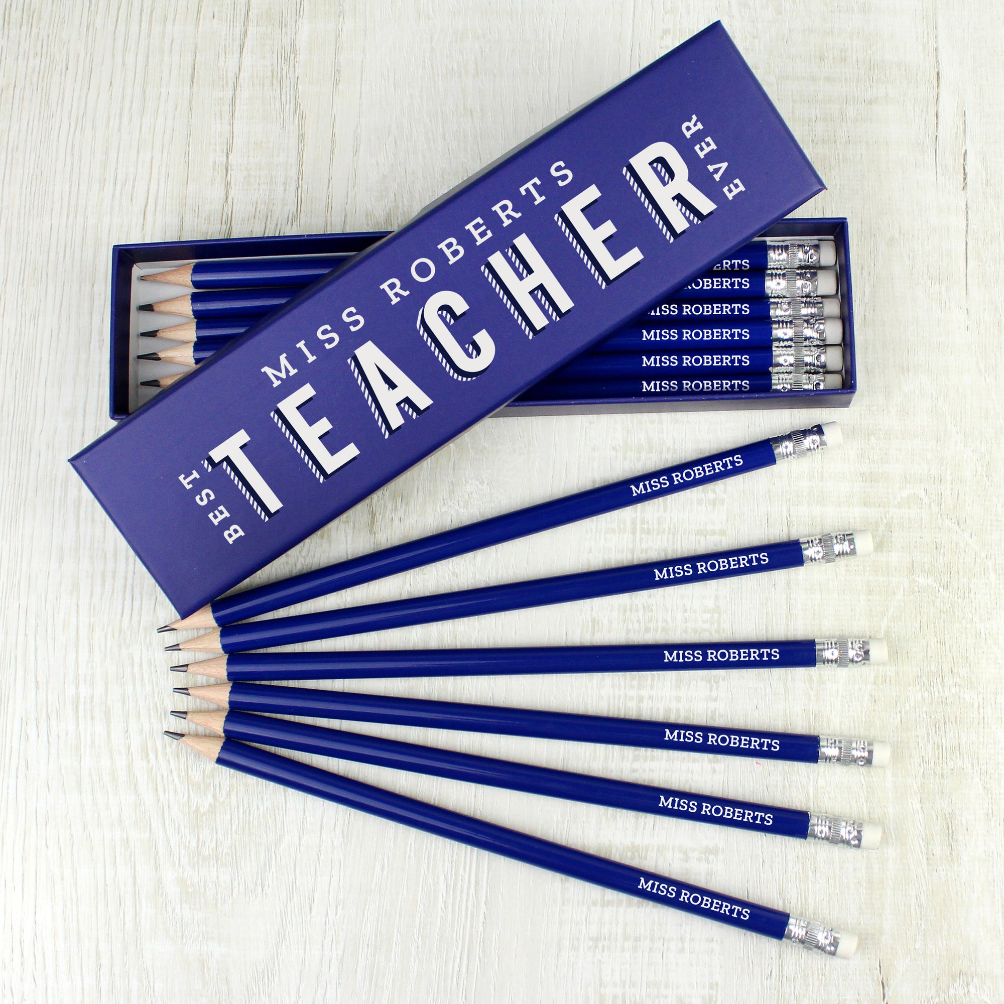 Image of a personalised box of 12 personalised pencils. The box is dark blue and can be personalised with a teacher’s name which will be followed by the fixed text of Best Teacher Ever which is printed in white modern uppercase letters. Inside the box has 12 HB pencils with a dark blue outer and a small eraser at the end. Each pencil will also be personalised with the teacher’s name in white uppercase letters.