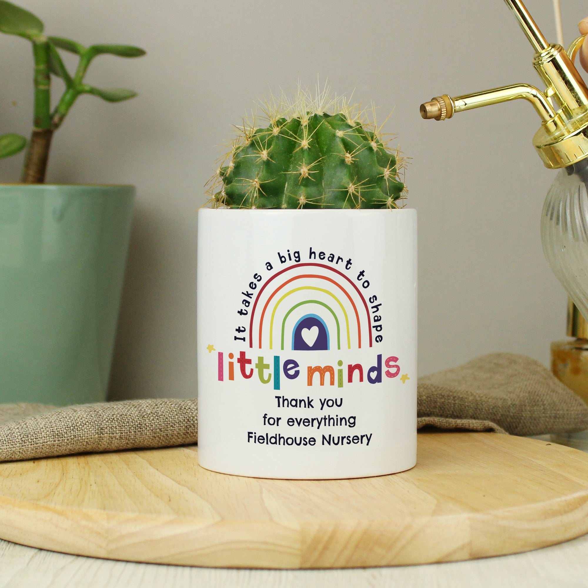 Image of a white ceramic pot with the text 'it takes a big heart to shape little minds' printed around a multicoloured rainbow. Directly below the pot can be personalised with your own text over up to 3 lines as a thank you gift for a teacher or teaching assistant.