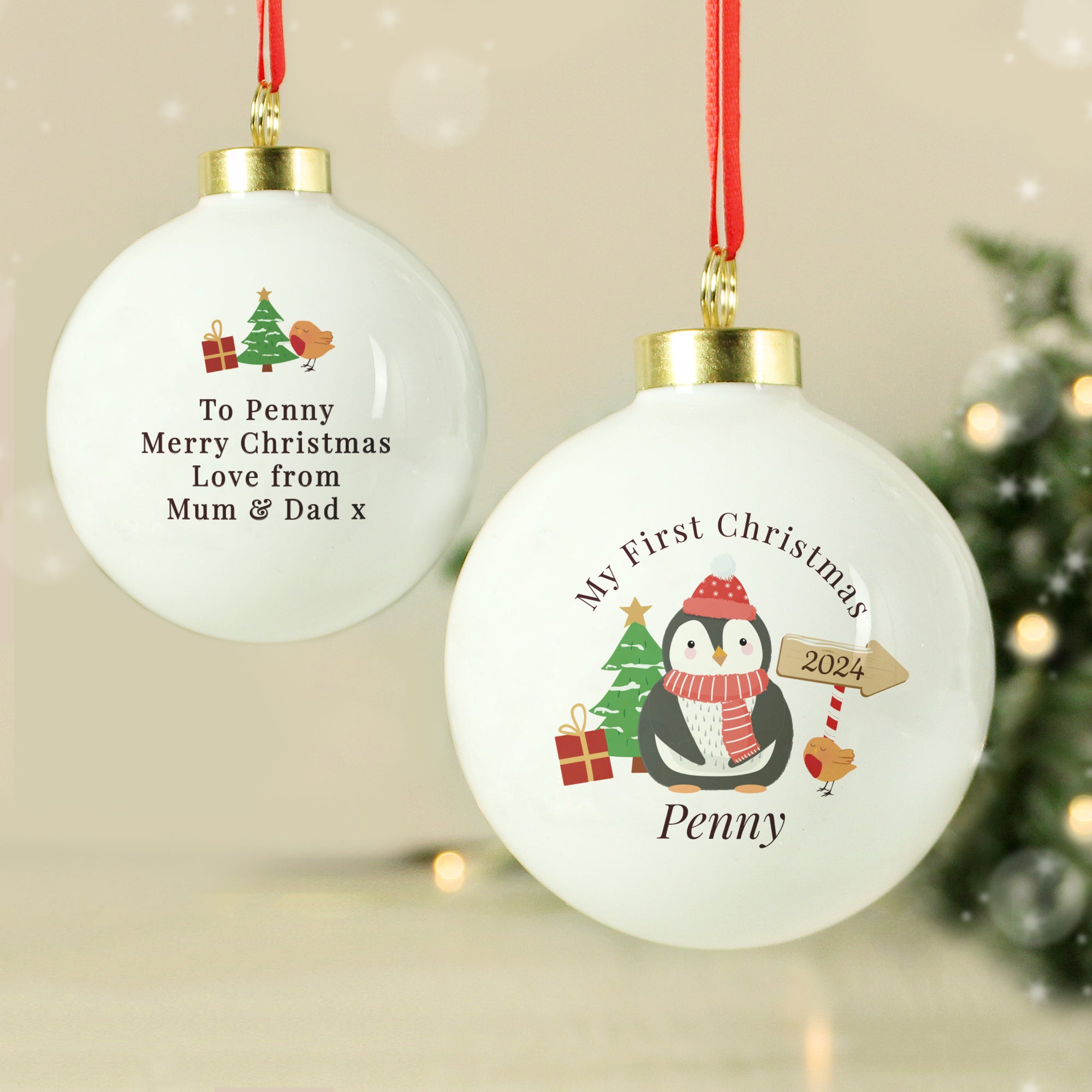 Image of the front and back of a personalised Christmas bauble. The bauble is white, the front features an image of a penguin with a hat on and scarf on. There is a small tree and gifts next to the penguin and an arrow sign with a year. Above the penguin in black text is ‘My First Christmas’ and below the penguin you can add a name. The back of the bauble has a small red and white candy cane and below it you can add your own message which will be printed in a black font.