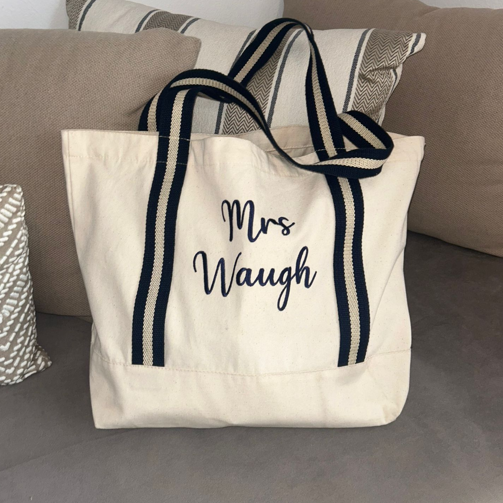 Image of a natural coloured tote bag with navy blue straps that has been personalised with a name embroidered in navy thread. The bag is available with four different strap colours, amber, red, navy and sage green and will be personalised in a matching thread colour.